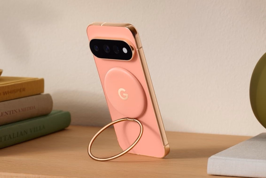 Un Pixel 11 en coral apoyado sobre un escritorio usando el Ring Stand desplegado como soporte