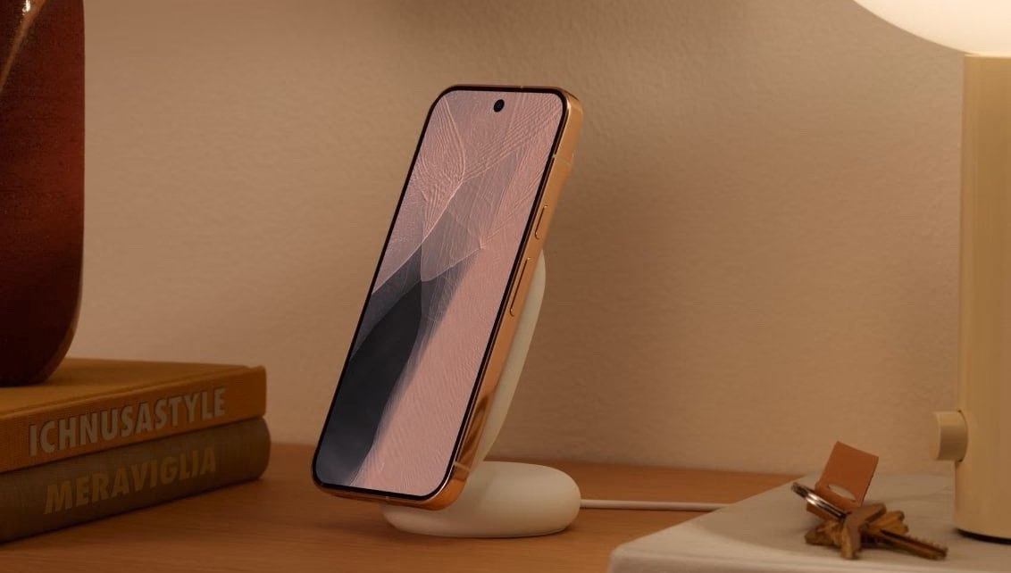 El Pixelsnap Charger Stand con un Pixel 11 cargando sobre una mesa de luz junto a una lámpara