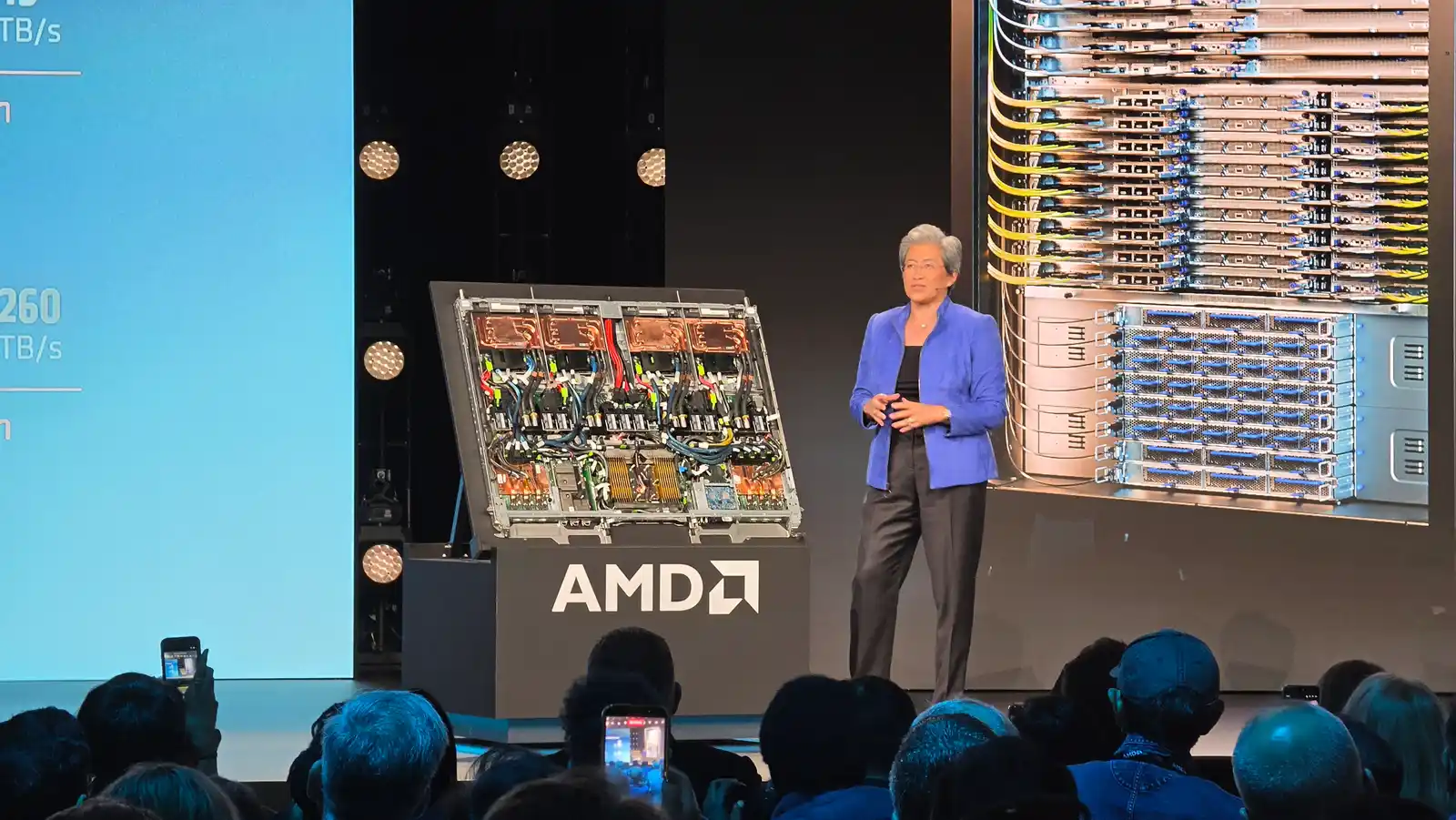 Lisa Su en el escenario de AMD junto a un nodo de servidor Instinct abierto, con un rack Helios en la pantalla de fondo