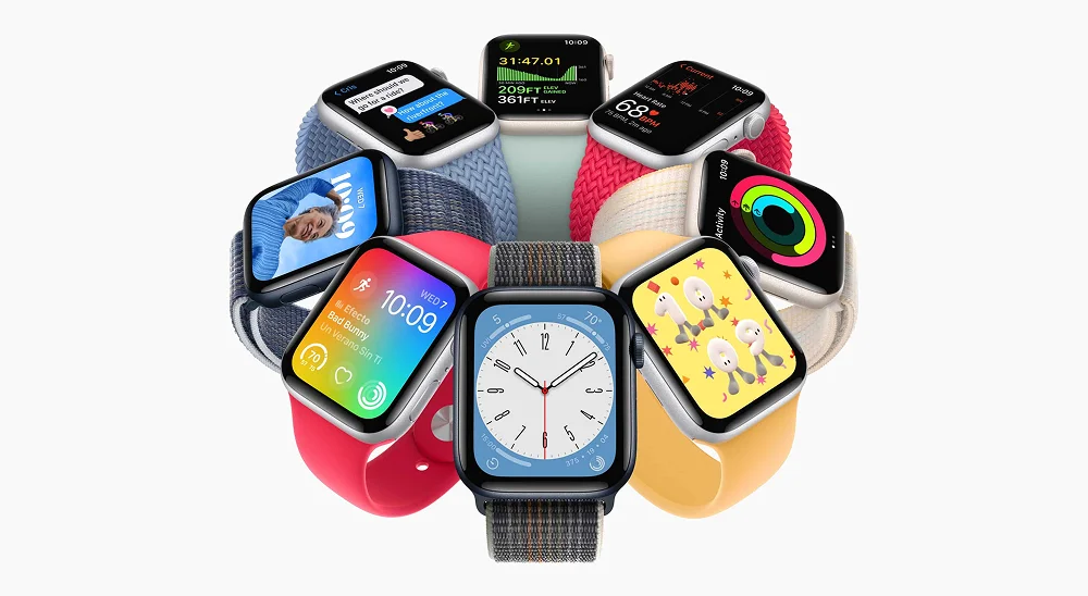 Múltiples Apple Watch SE 3 dispuestos en círculo, destacando la variedad de esferas de watchOS y diferentes colores de correas deportivas y trenzadas.