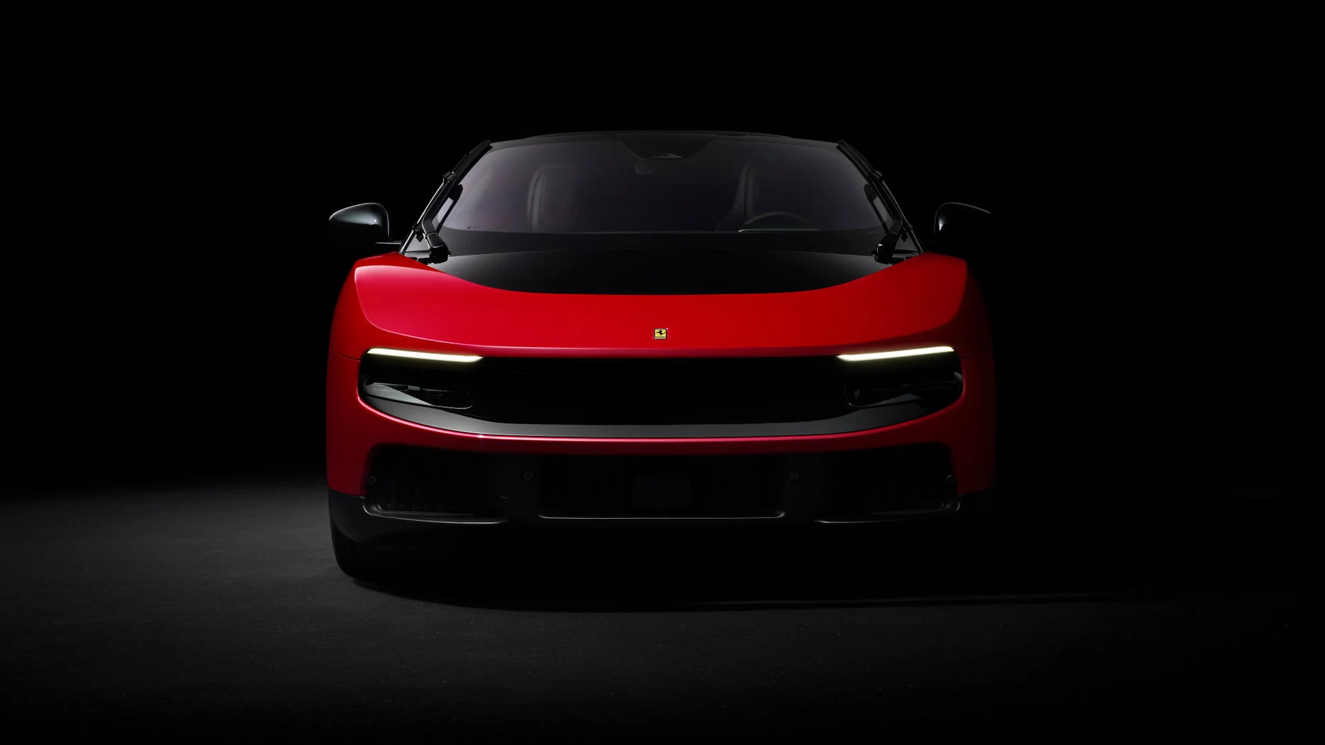 Front view of the Ferrari Luce in red on a black background, showing the continuous horizontal LED bar and the absence of traditional headlights
