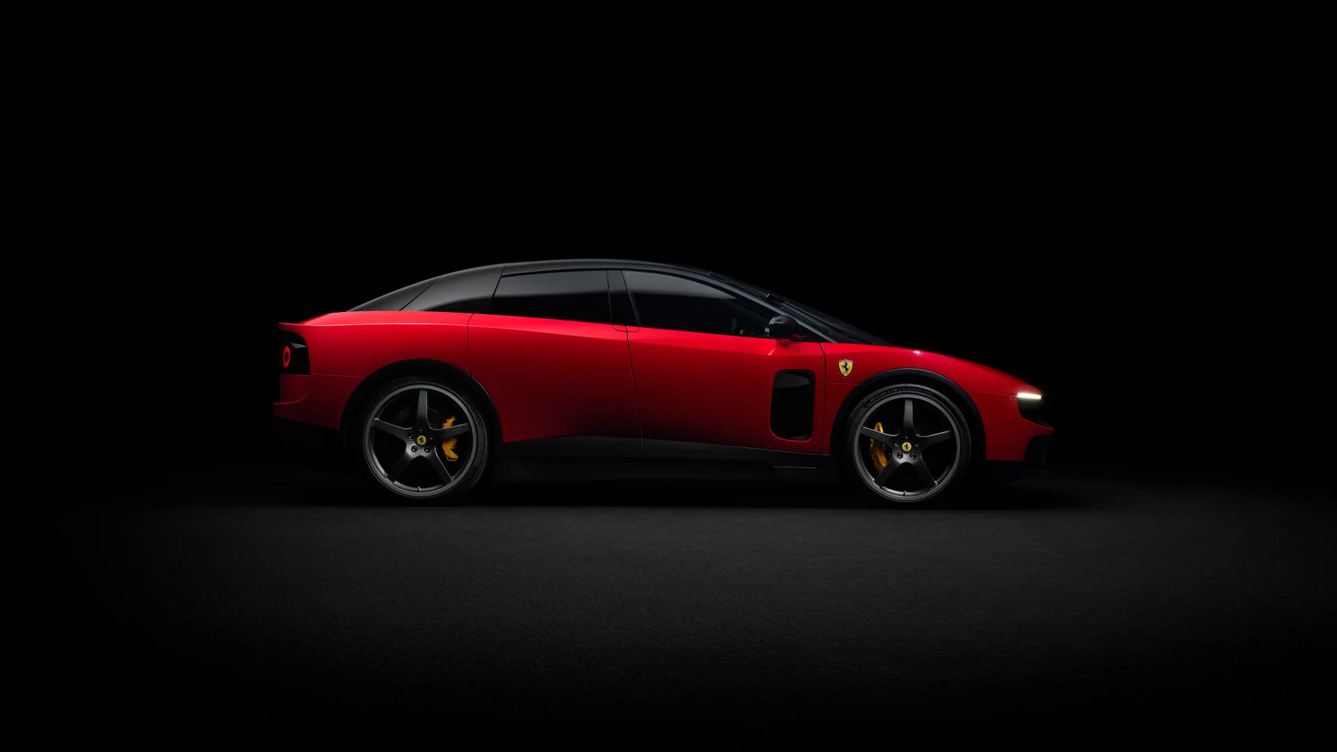 Side profile of the Ferrari Luce in Rosso Corsa red, photographed in studio with black background, showing the full fastback silhouette with descending black roof and five-spoke wheels