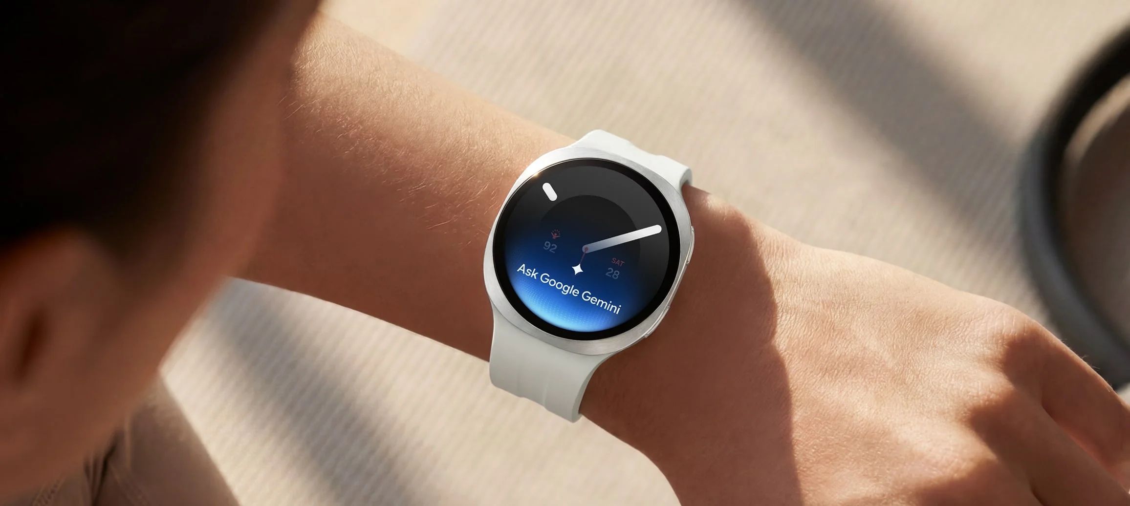 El Galaxy Watch 9 blanco en la muñeca mostrando la indicación Ask Google Gemini sobre la esfera
