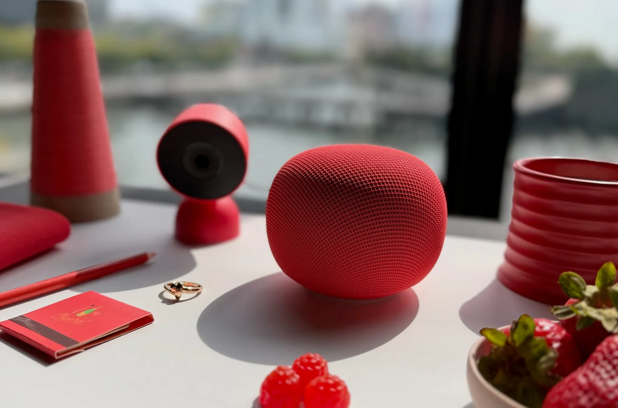 Google Home Speaker en color Berry sobre una mesa junto a una ventana