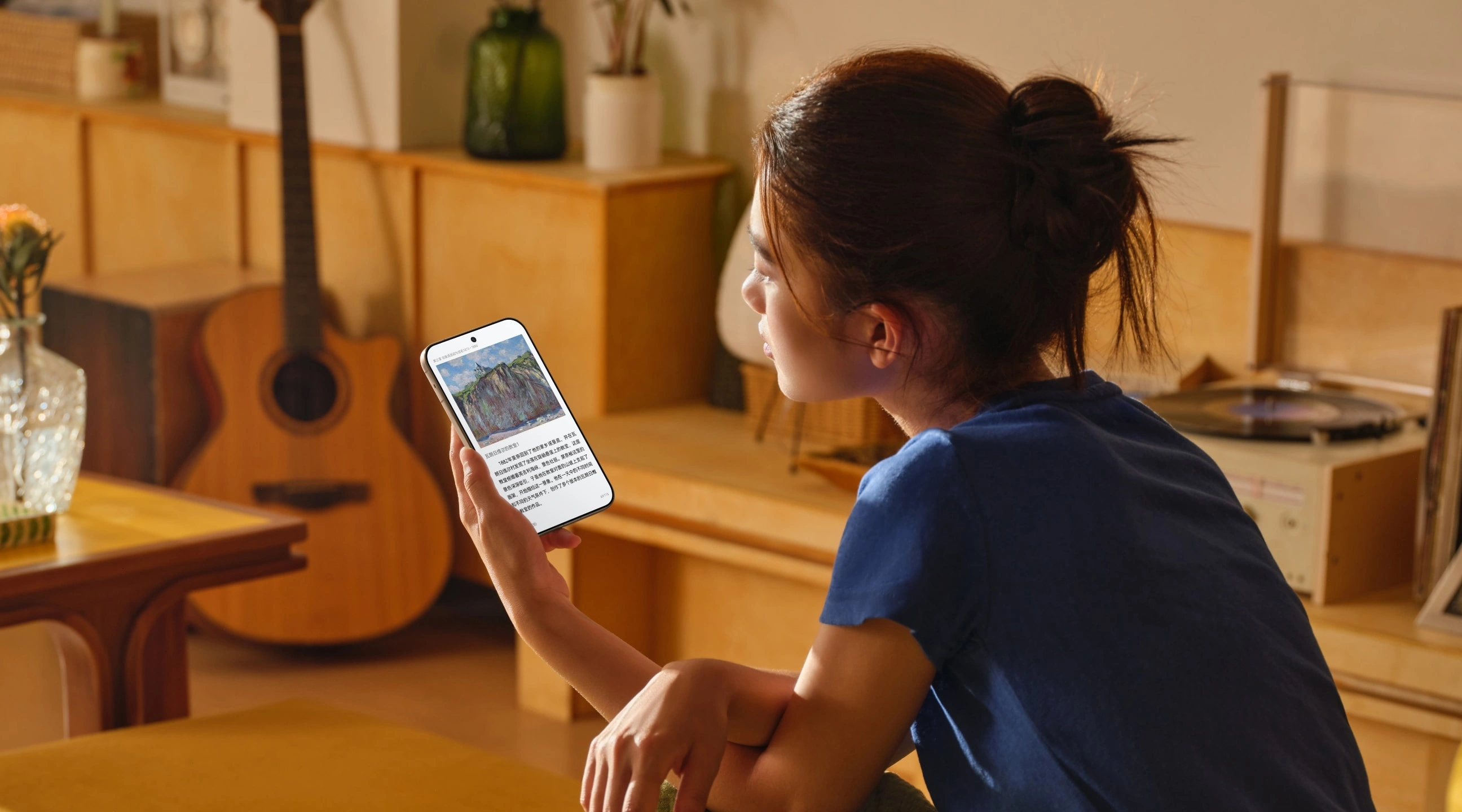 Woman reading an article on the Pura X View while sitting in a room with a guitar and record player