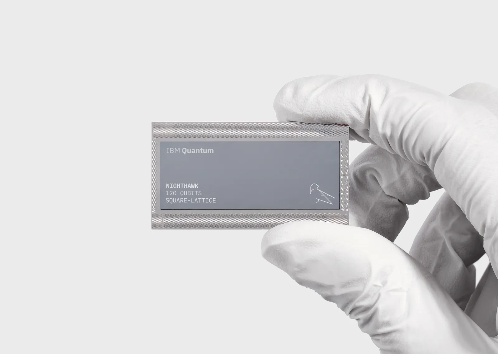 Una mano con guante sostiene el chip IBM Quantum Nighthawk de 120 qubits con estructura de red cuadrada.