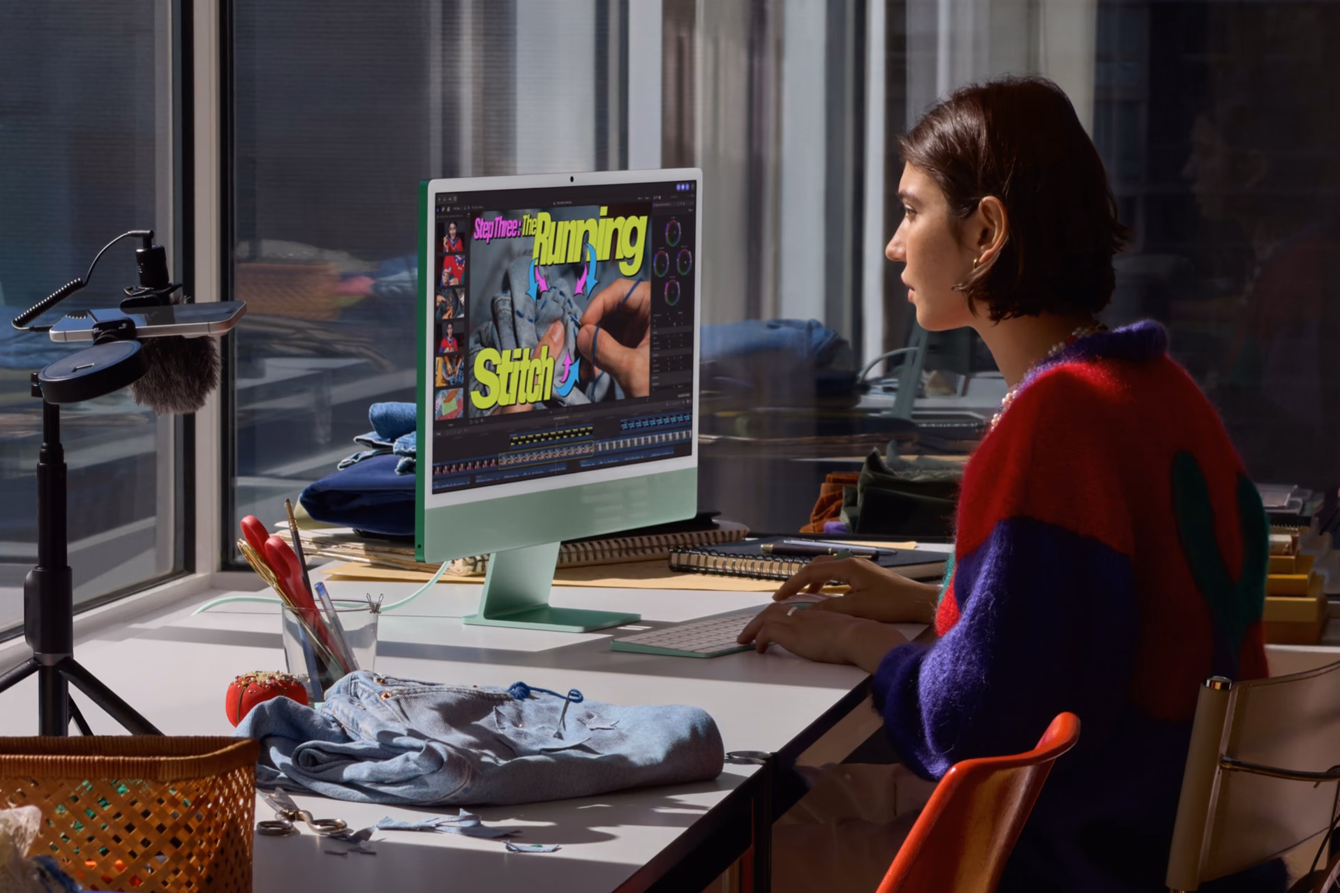 A person edits video on a green iMac next to fabrics