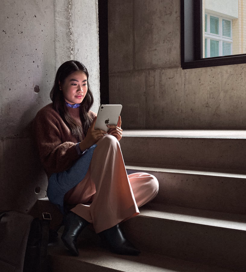 A person uses the iPad mini while sitting next to a bright window