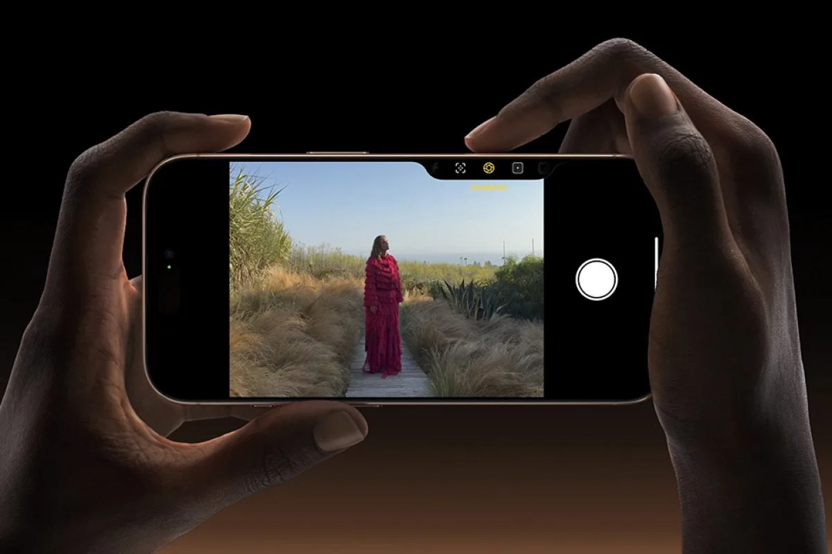 Dos manos sostienen un iPhone en horizontal usando el botón Camera Control para tomar una foto
