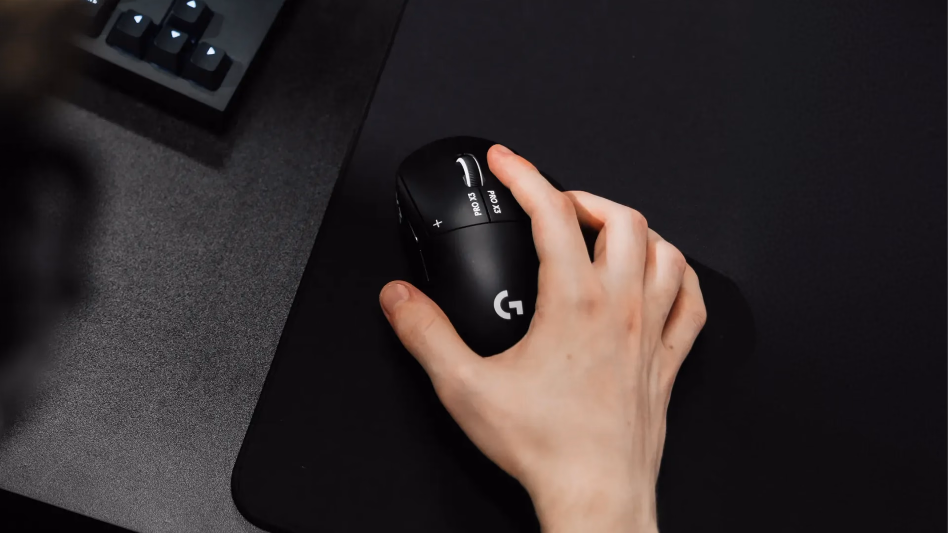 Hand on the PRO X3 SUPERSTRIKE seen from above, with a keyboard