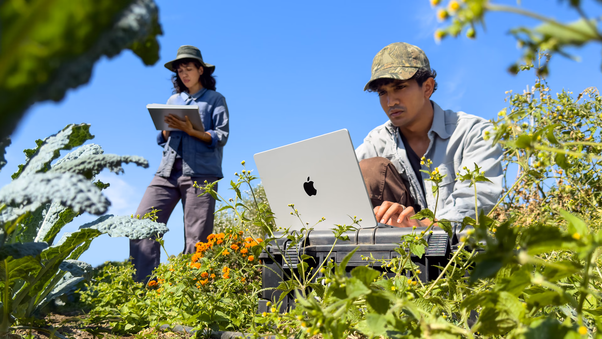 Two people use a MacBook Pro during field work