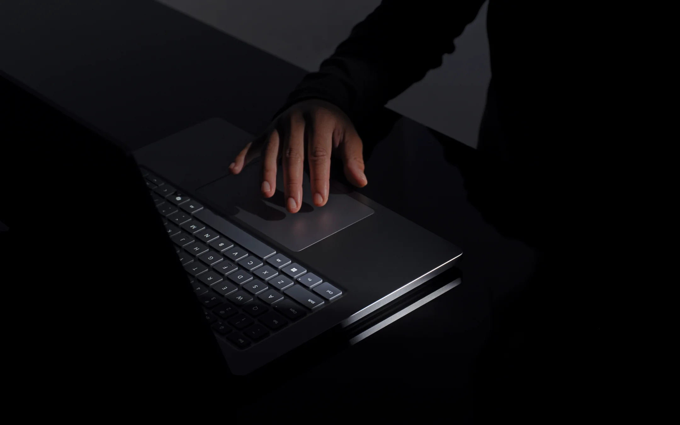 Mano usando el touchpad háptico de gran tamaño de la Surface Laptop Ultra en penumbra