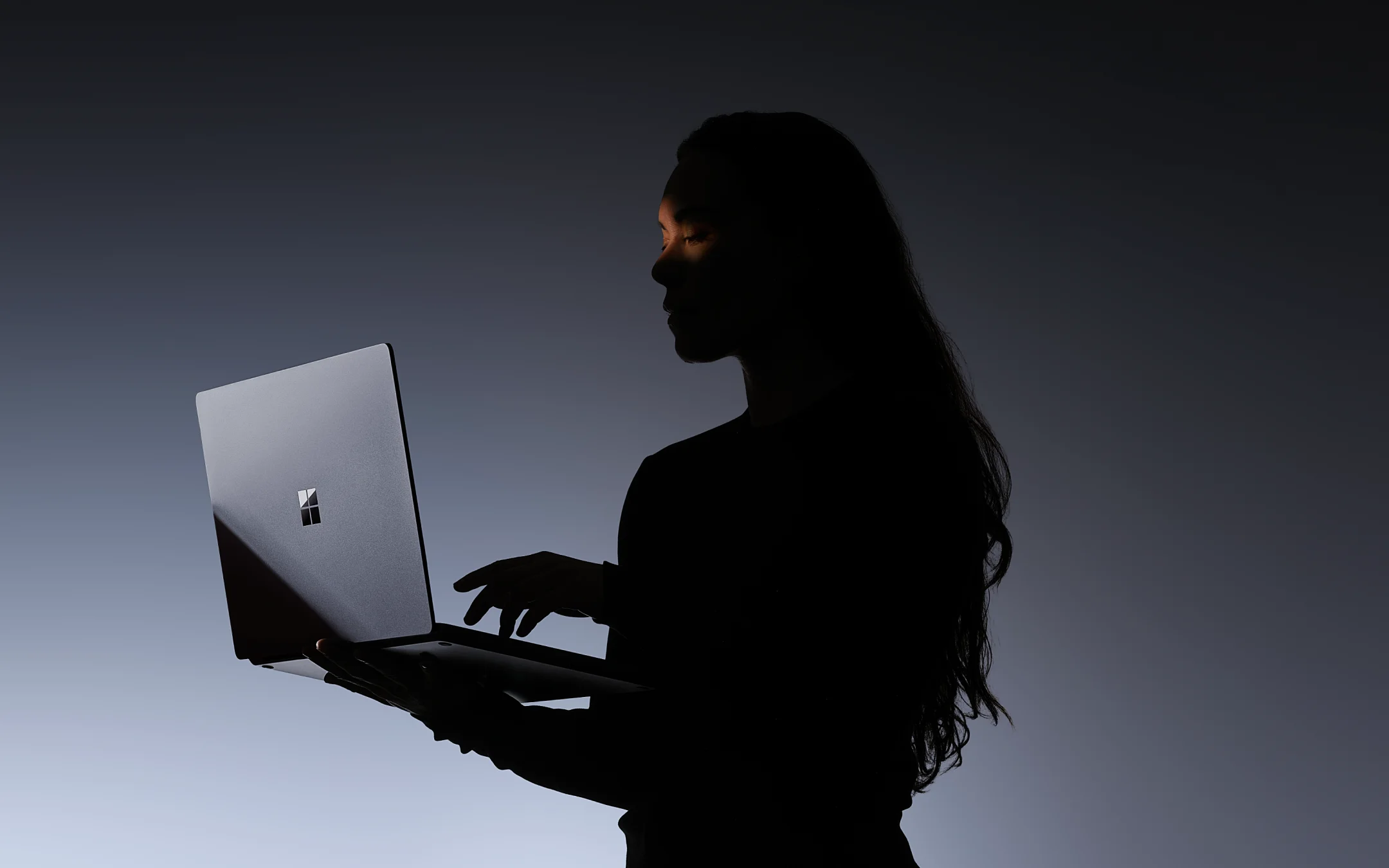 Silueta de una persona usando una Surface Laptop Ultra Platinum con el logo de Windows iluminado en penumbra