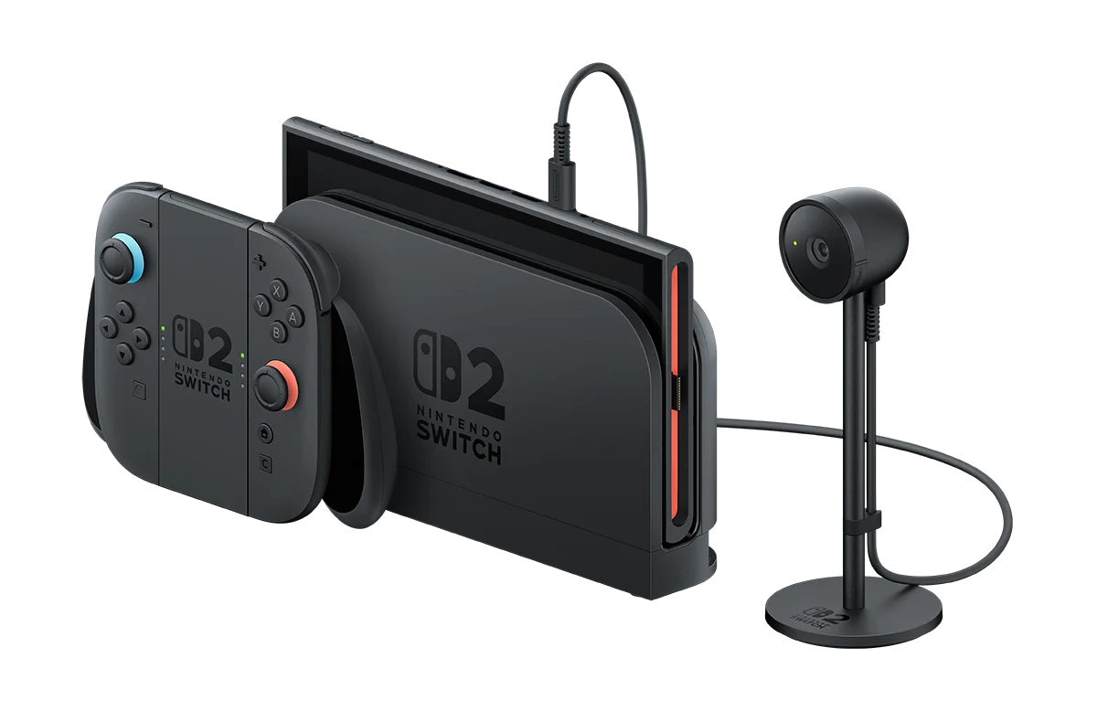 Nintendo Switch 2 with its magnetic Joy-Cons attached, next to the dock and accessory camera on its stand connected by cable, all in black on a dark background