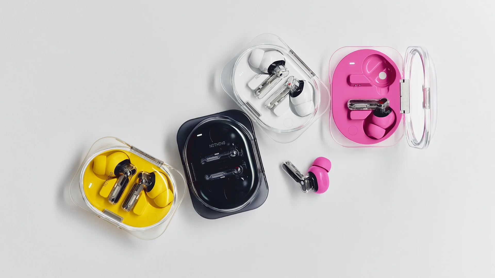 Los cuatro estuches del Nothing Ear (3a) en amarillo, negro, blanco y rosa vistos desde arriba con los auriculares adentro