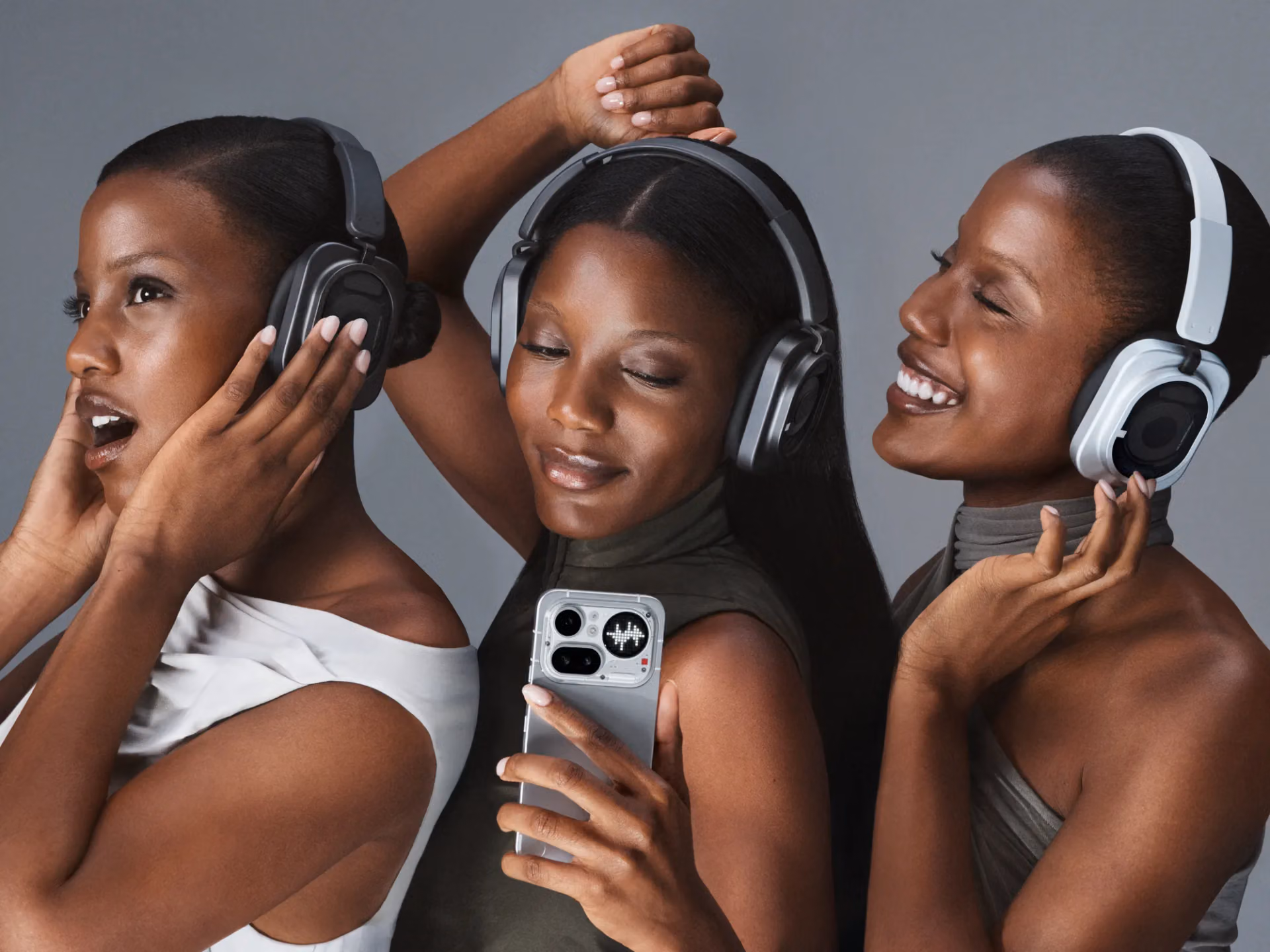 Three women wearing Nothing headphones, two dark and one white, with a phone in hand