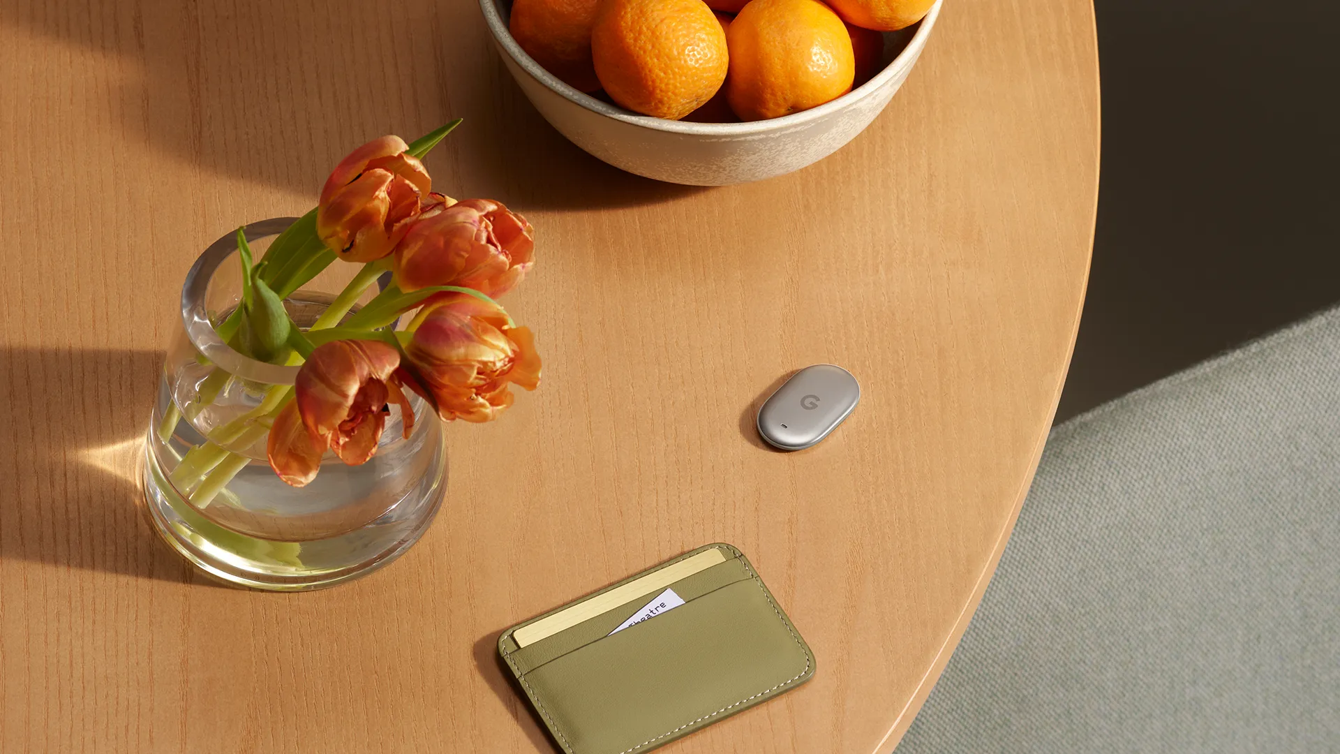 El Pixel Tag apoyado sobre una mesa de madera junto a un florero con tulipanes y una tarjetera de cuero