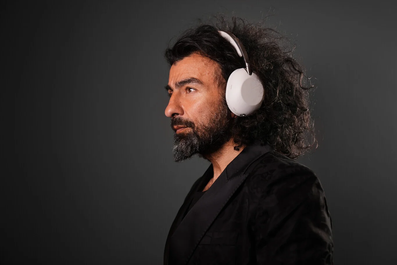 Young man with curly hair wearing the Sony 1000X The Collexion headphones in Platinum color in profile against a dark background